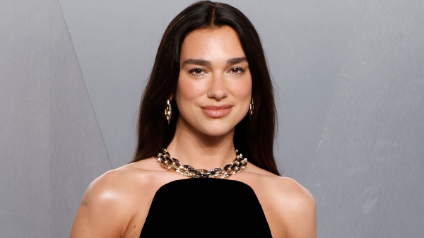 Dua Lipa poses in a black dress. She wears her hair long.